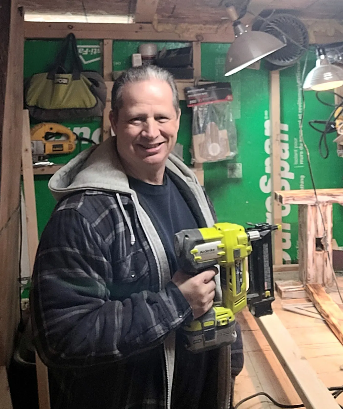 Rob, owner of Backyard DIY Builder, in his Prince George workshop holding a nail gun next to a torched stool