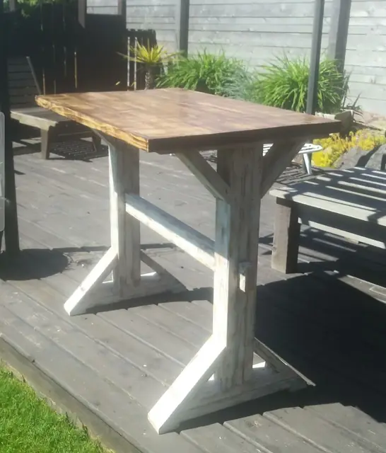 Counter-height rustic farmhouse table with white-washed base on an outdoor deck