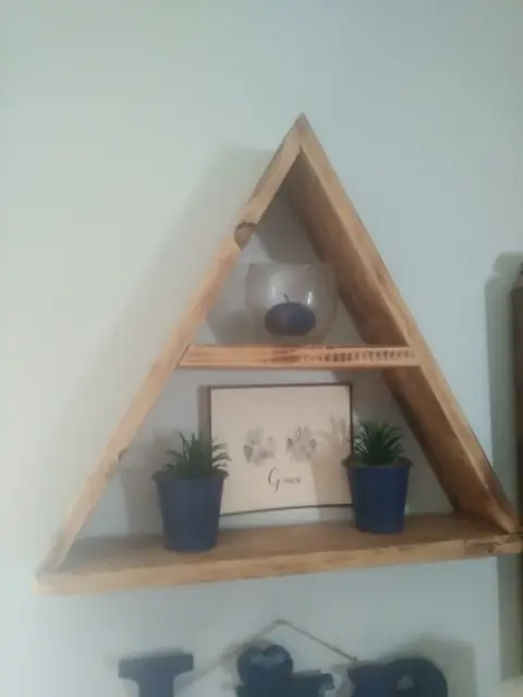 Triangle wall shelf with honey finish holding plants and decor